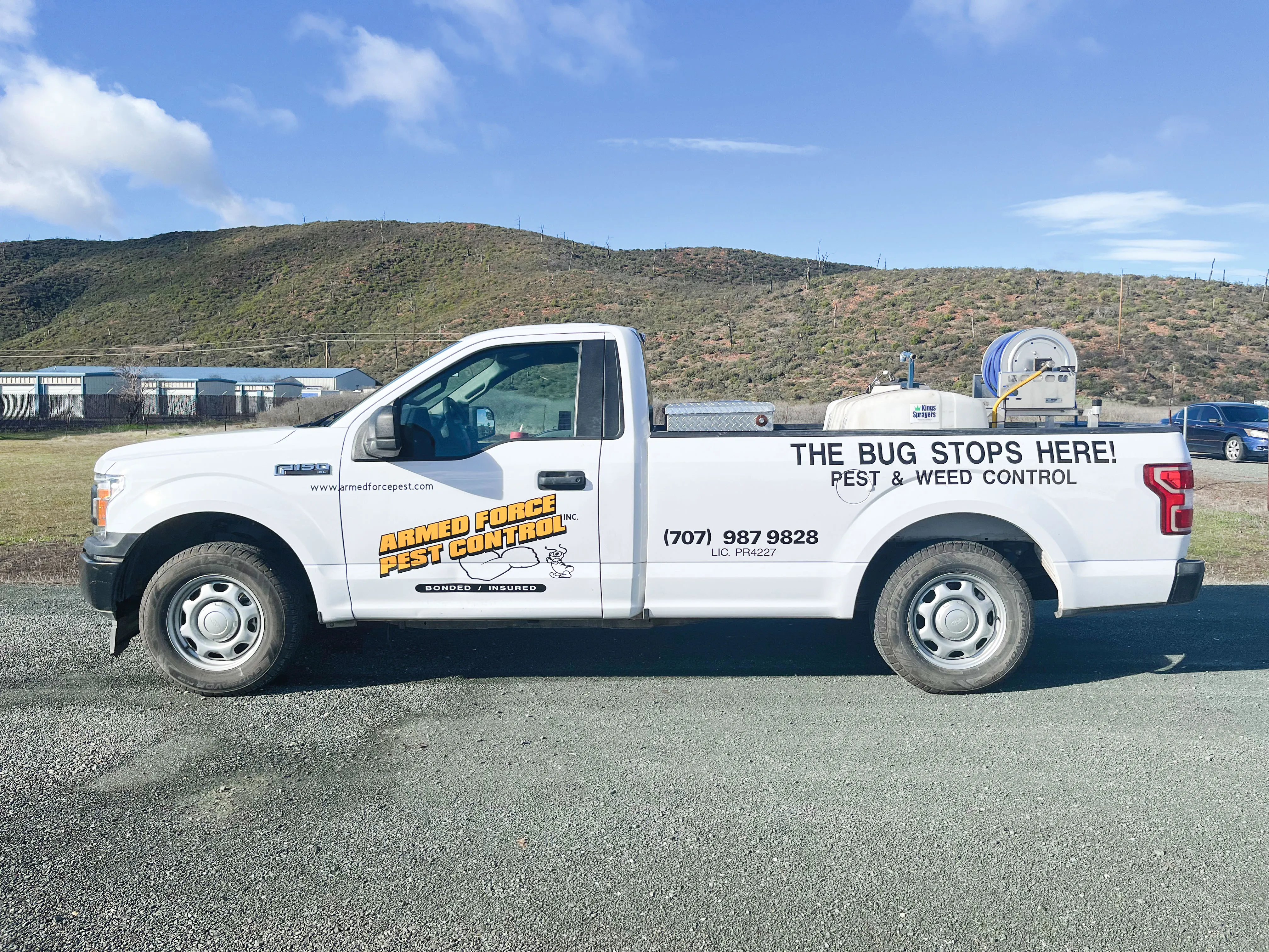 A white Armed Force Pest Control, Inc. truck parked on a gravel surface with hills in the background, displaying company branding and contact information.