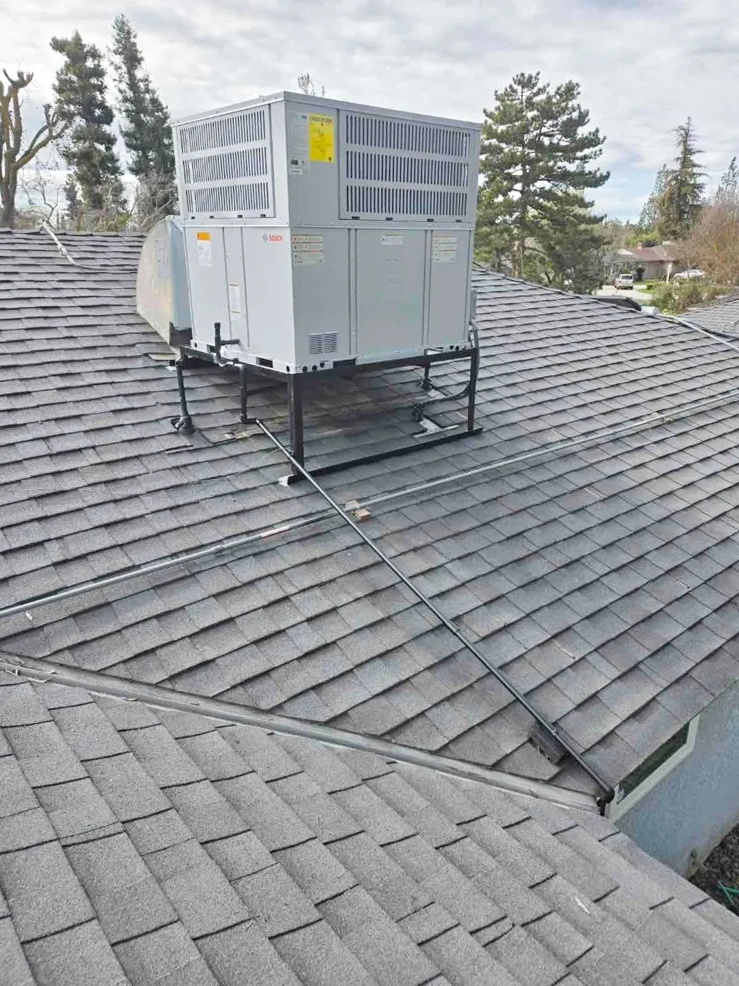 A rooftop HVAC unit installed on a shingled roof in Pleasanton by Art's Heating & Cooling, with trees and a neighborhood visible in the background.