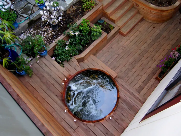 A wooden deck in San Francisco featuring a circular water feature surrounded by plants and flower beds, designed by Artisans Landscape Inc.