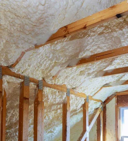 An image of an attic with wooden beams and spray foam insulation applied between them.