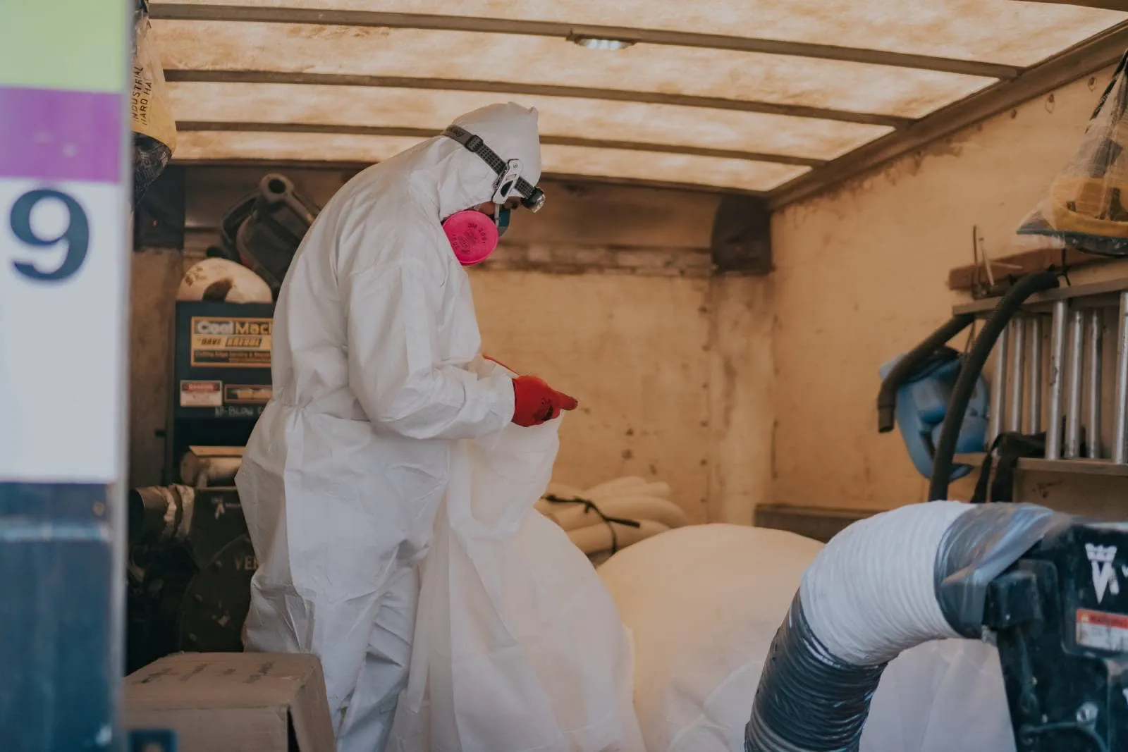 A worker in protective gear conducts an inspection inside an attic for AtticPros in Oakland.
