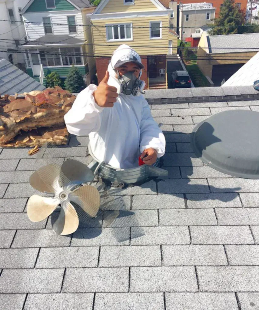 A worker from Atticare Construction, dressed in protective gear, gives a thumbs-up while installing attic ventilation on a roof in San Leandro.