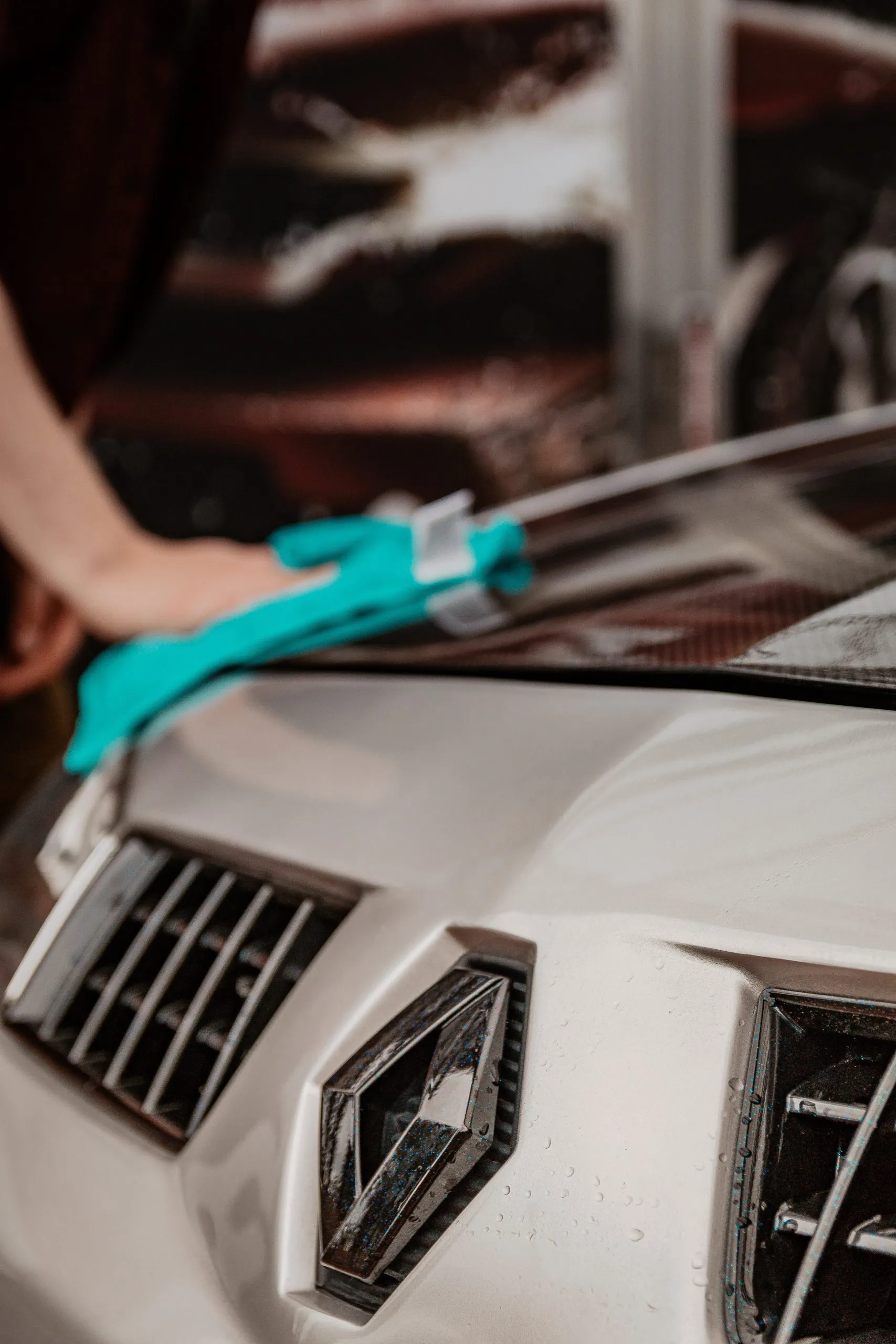 Close-up of a person polishing a car hood with a turquoise cloth at AutoShield Collision in Santa Clara, focusing on the front grille and emblem.