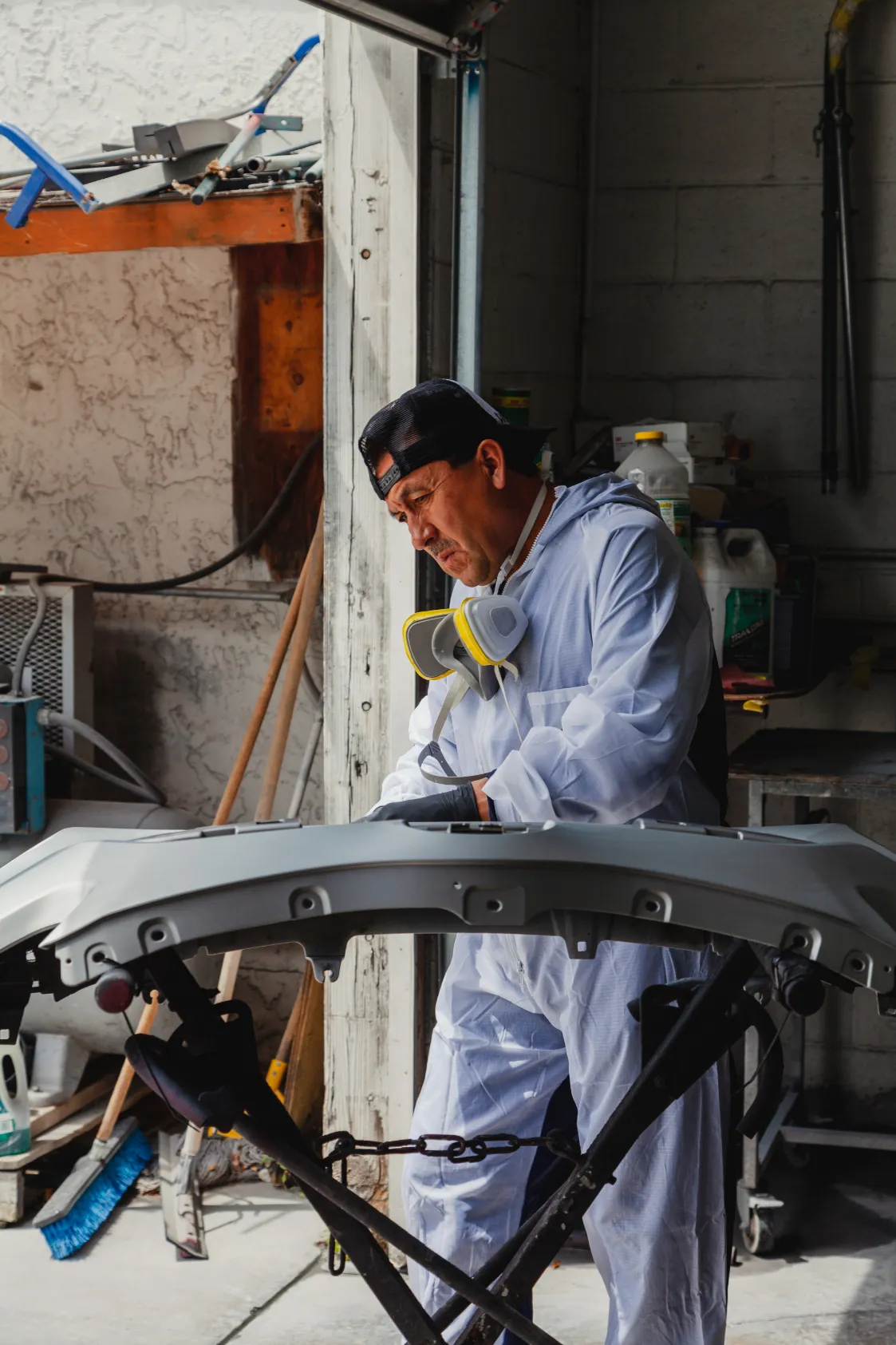 A technician carefully examines a vehicle bumper inside an AutoShield Collision garage in Santa Clara, wearing protective gear and focused on quality repair work.