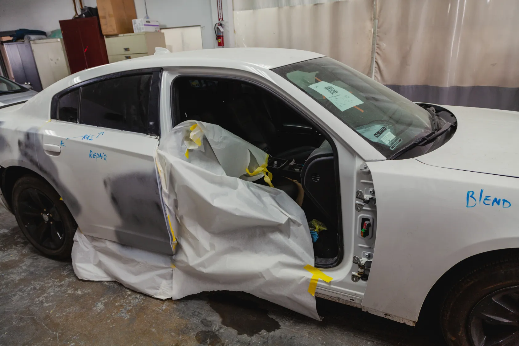 A white car undergoing repair at AutoShield Collision in Santa Clara, with protective paper covering and visible repair notes.