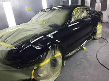 A car in a spray booth at AutoCollisionExperts in Sunnyvale, covered with protective masking and prepared for a professional paint job.