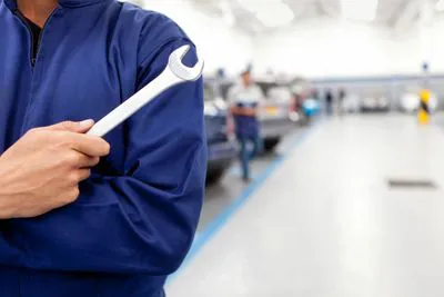 "Mechanic in blue uniform holding a wrench at AutoCollisionExperts shop in Sunnyvale."