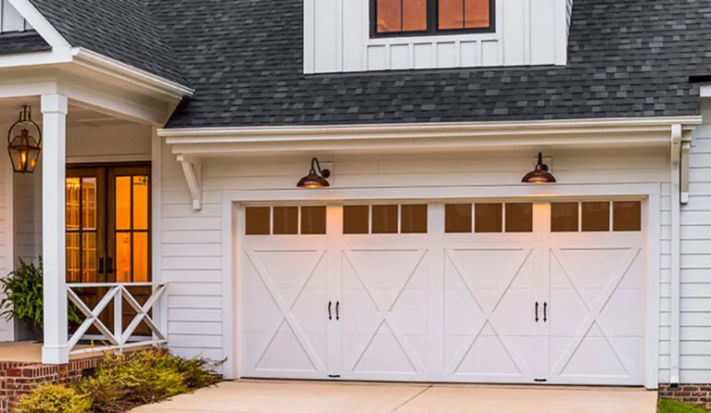 White garage door with windows and outdoor lighting on a white house, showcasing the craftsmanship of Automatic Garage Door Corporation in San Francisco.