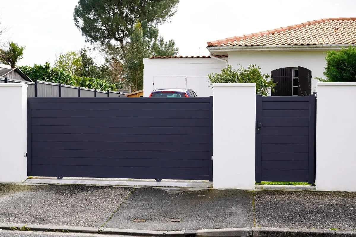 A modern, dark-colored automatic gate installed in front of a residential property with a car visible behind it.