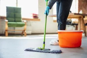 Person mopping a floor with a green mop next to an orange bucket, representing BA House Cleaning services in Castro Valley.