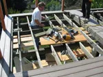 A construction worker building a wooden deck frame with various tools at a worksite.