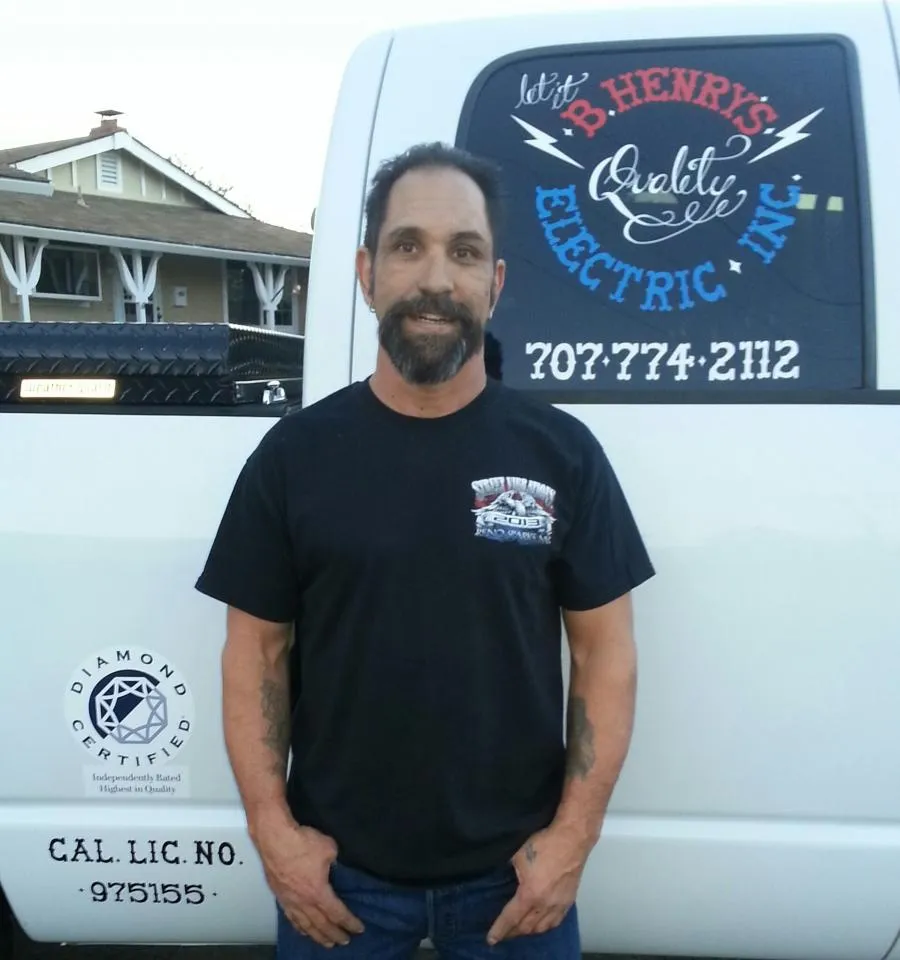 A man stands in front of a vehicle with the logo and contact information for B. Henry's Quality Electric Inc. visible on the side.