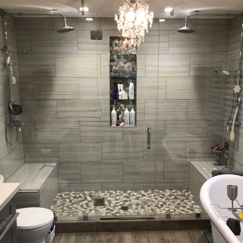 A modern bathroom featuring a glass-enclosed shower with dual showerheads, a tiled wall with built-in shelving, and a chandelier, showcased by B & L Glass in Santa Rosa.