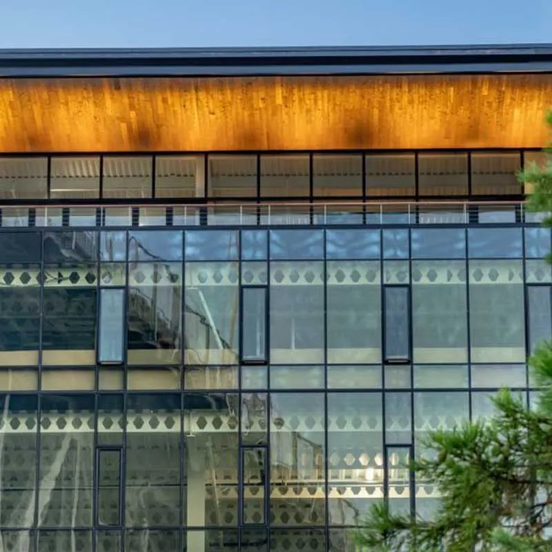 Close-up view of a modern building with large glass windows and a wooden roof, reflecting the sky and trees, created by B & L Glass in Santa Rosa.