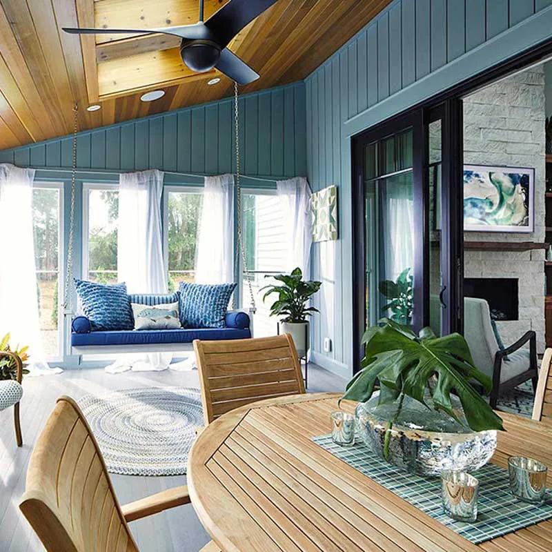 A modern room featuring large glass windows and doors by B & L Glass in Santa Rosa, showcasing a wooden ceiling, blue walls, a round wooden table with plants, and a comfortable sitting area.