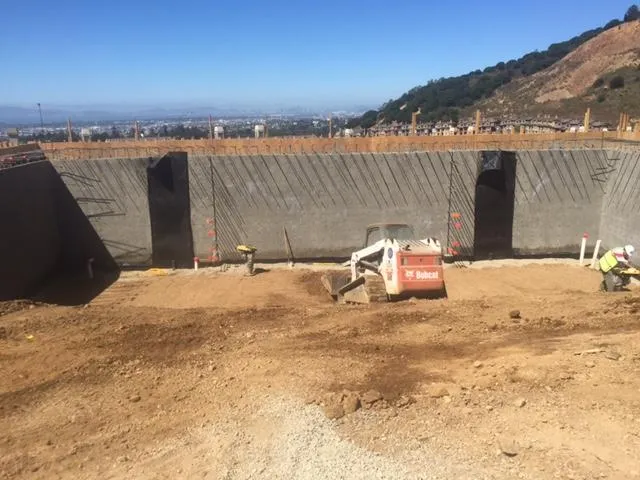 Construction site with heavy machinery operated by Bay Area Drainage, Inc., featuring unfinished concrete walls and a clear blue sky in Moraga.