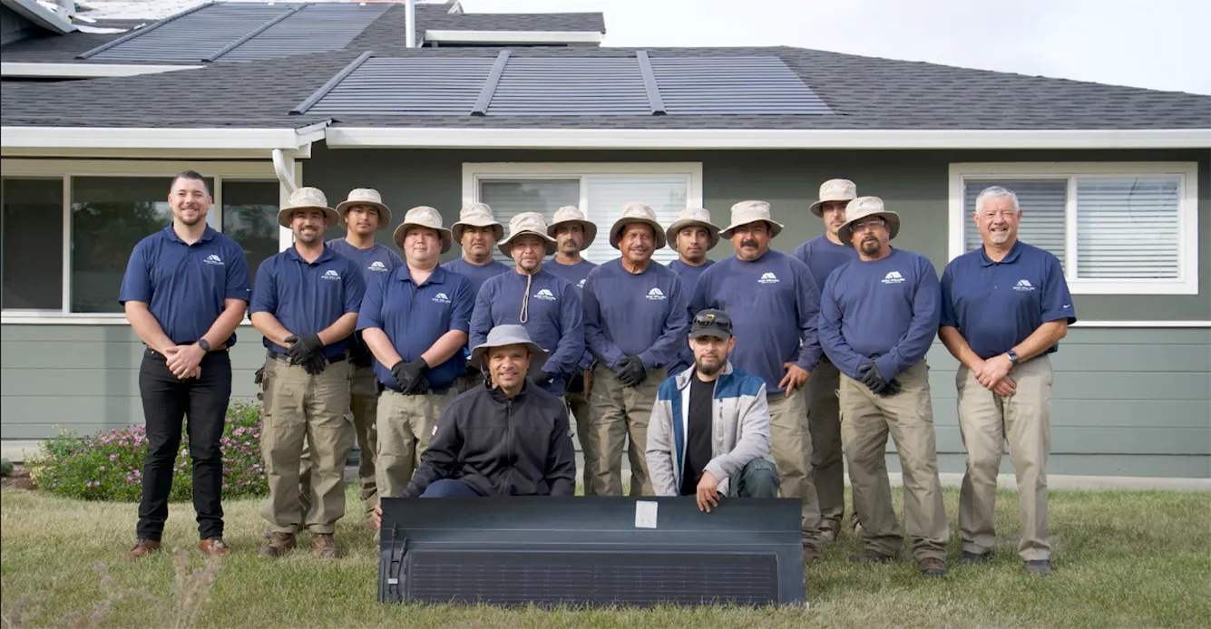 A group of Bay Valley Roofing employees in Concord posing in front of a house with solar panels, wearing matching uniforms and hats, showcasing a strong commitment to roofing excellence.