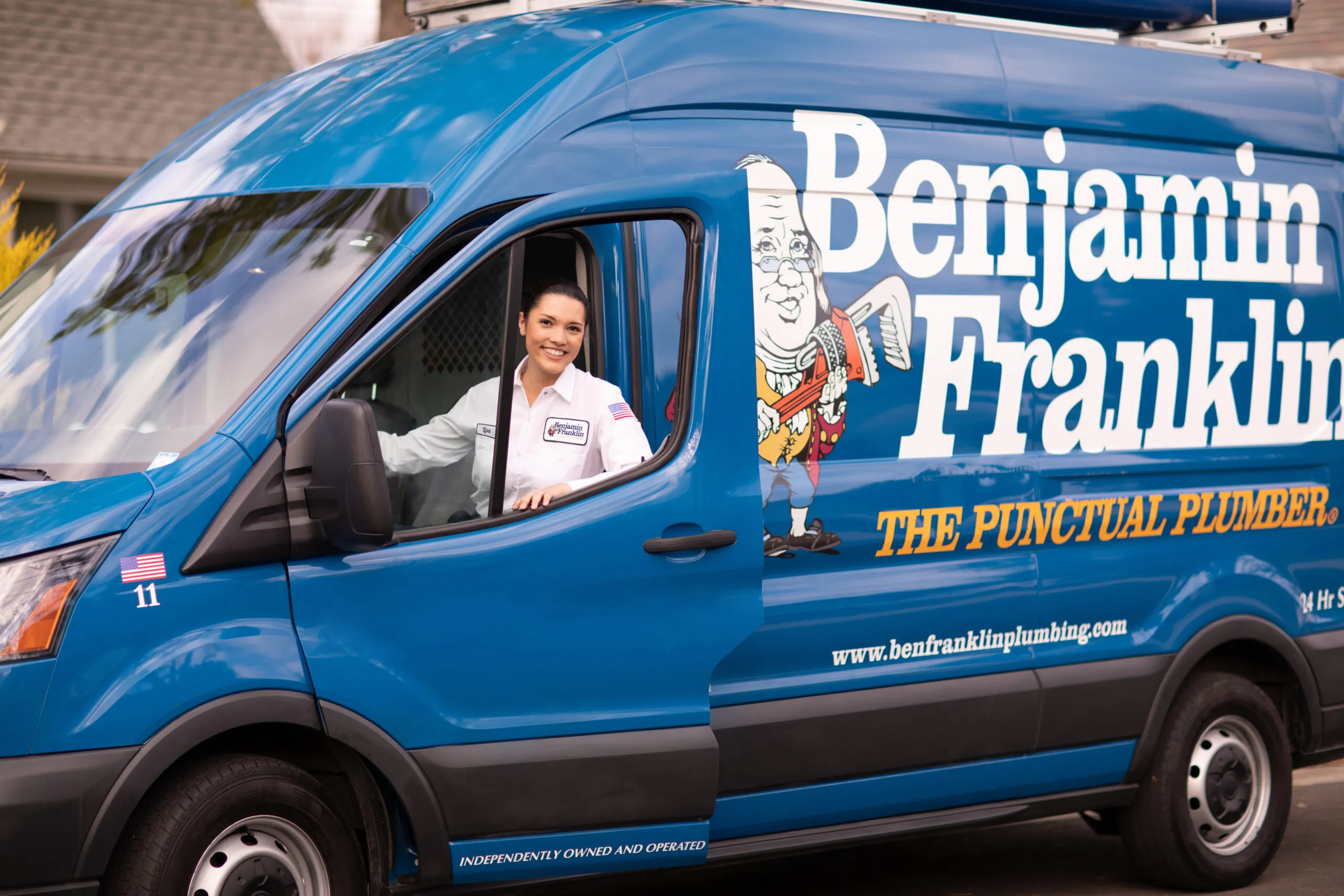 A technician in a blue Benjamin Franklin Plumbing van poses while sitting in the driver's seat, ready to serve Novato residents.