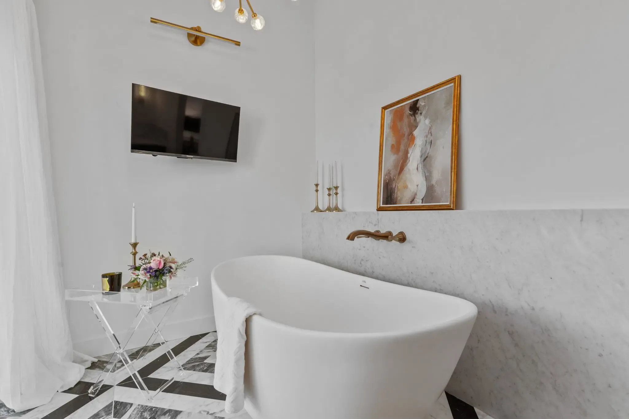 A modern bathroom with a freestanding white bathtub, a mounted TV, abstract painting, and elegant décor, showcasing Best Construction's design in San Jose.