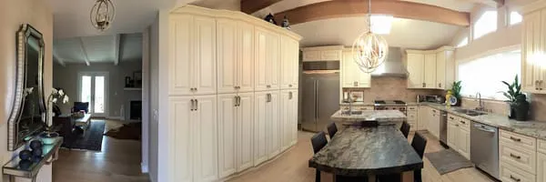 A panoramic view of a modern kitchen with cream-colored cabinets, a central island with a dark countertop, stainless steel appliances, and a cozy adjacent living area, completed by Best Construction in San Jose.