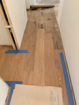 A hallway in the process of hardwood flooring installation, with some wooden planks and protective paper in place.