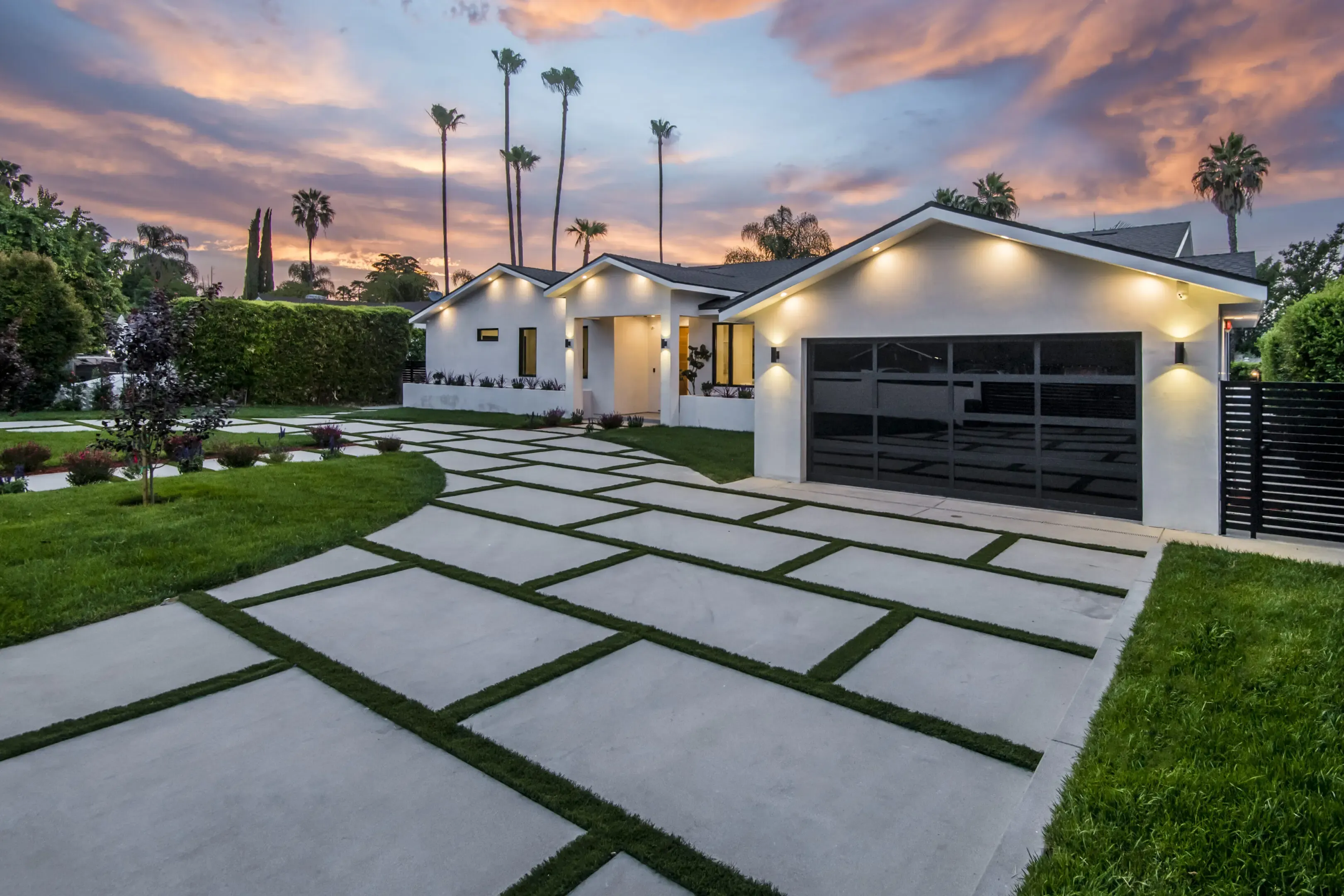 A modern house with a well-manicured lawn and geometric driveway at sunset, constructed by Best Construction in San Jose.