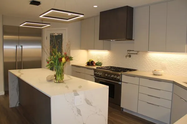 A modern kitchen with sleek cabinetry, a marble island, and geometric lighting, featuring high-end appliances.