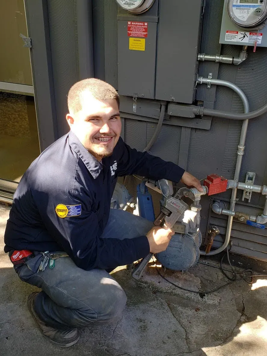 A plumber from BigBluePlumbing in Alameda working on outdoor utility equipment, smiling while holding a wrench.