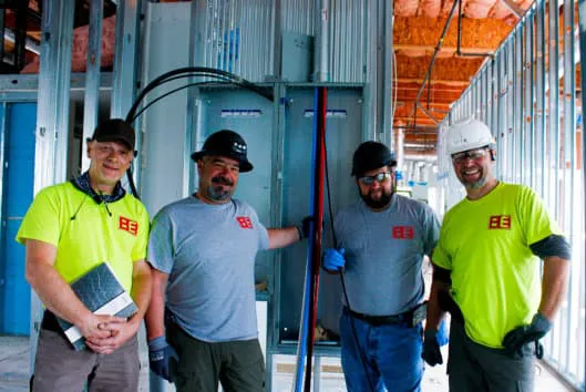 Four electricians from Bit Electrical Inc., wearing safety gear and standing in front of an electrical setup in a building under construction in Daly City.