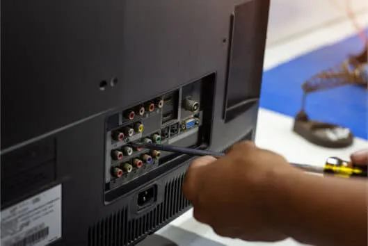 A person connecting cables to the back of an electronic device, illustrating the meticulous process of cable management by Bit Electrical Inc. in Daly City.