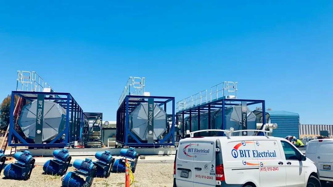 Bit Electrical Inc. vans parked in front of large industrial equipment under a clear blue sky in Daly City.