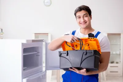 An electrician from Bit Electrical Inc. in Daly City smiling while holding an open toolbox next to a refrigerator with its door open.