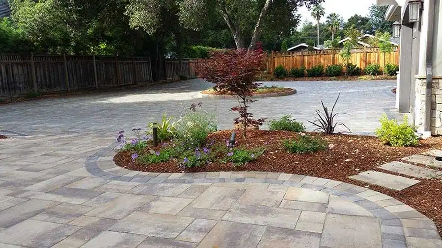 A beautifully landscaped garden with stone pavers and a variety of plants, designed by Black Diamond Paver Stones & Landscape, Inc. in San Jose, featuring a curved stone pathway and a wooden fence in the background.
