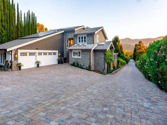 A beautifully paved driveway leading to a modern home, emphasizing the craftsmanship of Black Diamond Paver Stones & Landscape, Inc. in San Jose, with a scenic background of mountains and greenery.