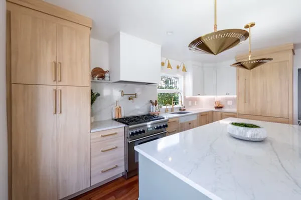 A modern kitchen featuring light wood cabinets, a white marble island, and stylish pendant lighting, showcasing design options from Budget Blinds of Central Marin and South Marin in Rohnert Park.