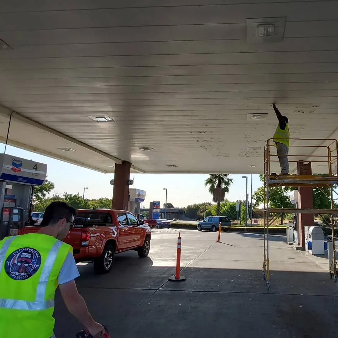 Workers from CG Coatings Inc performing maintenance on the ceiling of a gas station in Fairfield, with one person on a scaffold and another on the ground.
