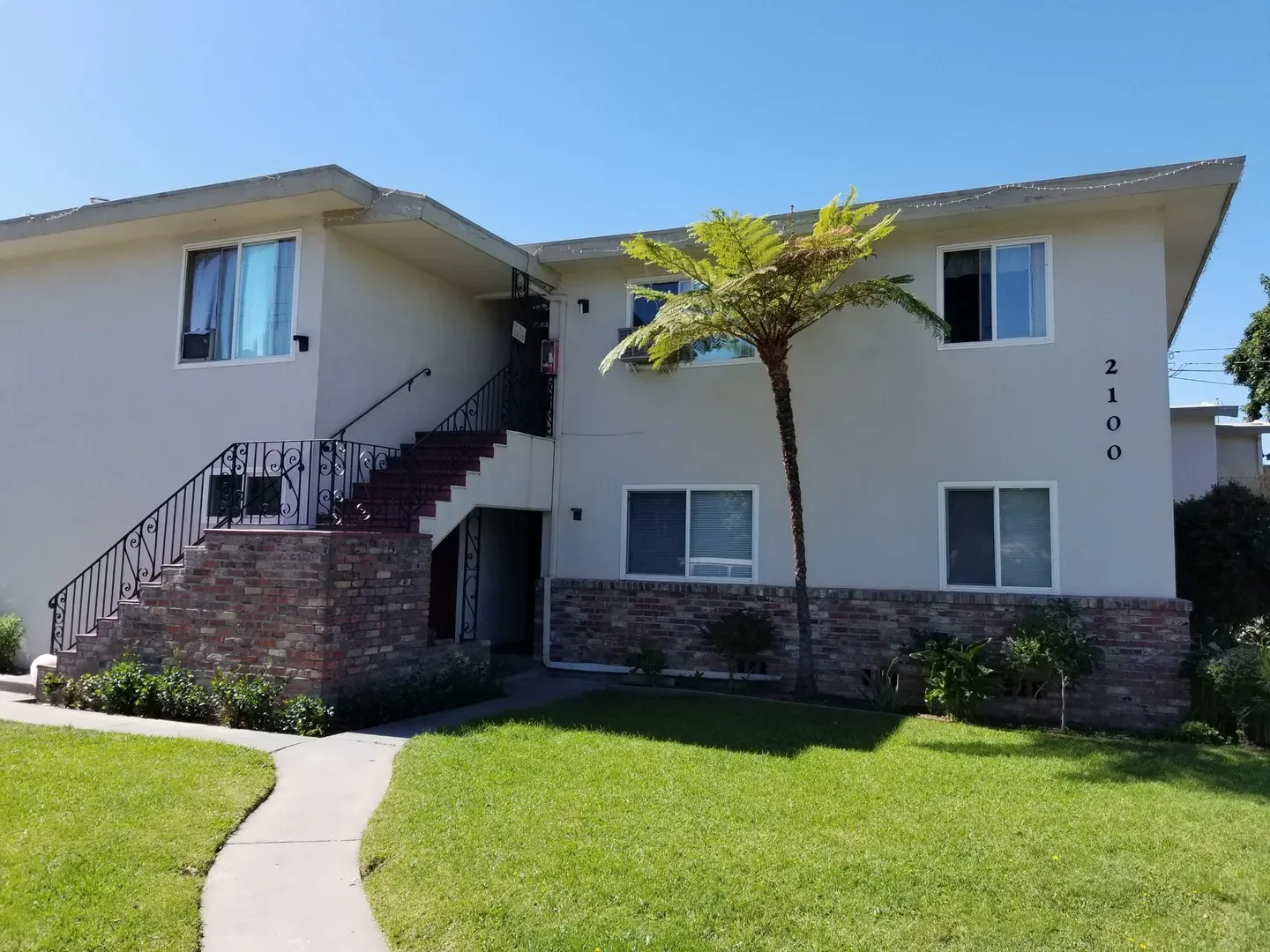 A two-story residential building with white walls, brick accents, and a palm tree, managed by CM Property Management Inc. in San Jose.