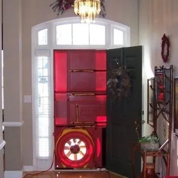 A door with a red blower door test setup inside a house, used to measure air leakage.
