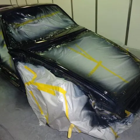 A car in the painting process at Cal Auto Body, Daly City, covered and taped for protection with areas prepared for paint application.