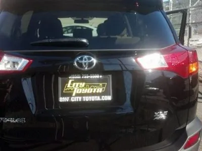 Rear view of a black Toyota SUV in a parking area, with a dealership license plate from City Toyota displayed.