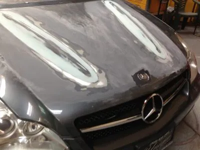 A car hood undergoing restoration at Cal Auto Body in Daly City, showing areas with primer applied for repair.
