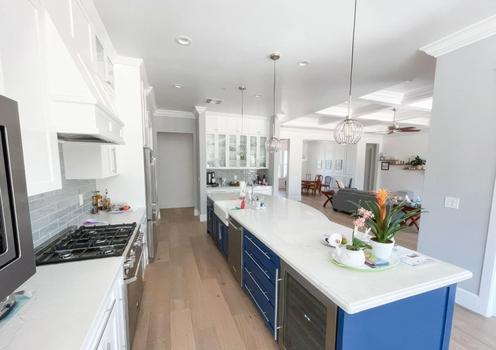 A modern kitchen with a long island featuring blue cabinetry, pendant lighting, and white countertops, designed by Cal Pro Trim & Finish in Sacramento.