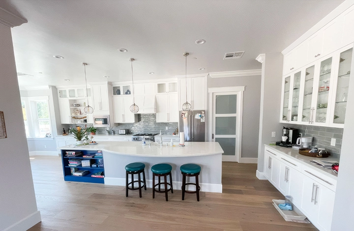 A modern kitchen with white cabinetry, a central island with teal stools, and stainless steel appliances, showcasing the craftsmanship of Cal Pro Trim & Finish in Sacramento.