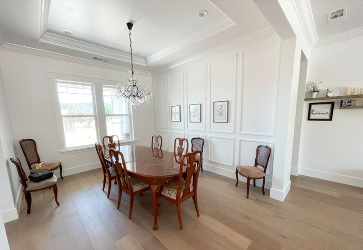 A well-appointed dining room featuring white walls with decorative molding, a wooden dining table and chairs, a chandelier, and large windows, exemplifying the expert craftsmanship of Cal Pro Trim & Finish in Sacramento.