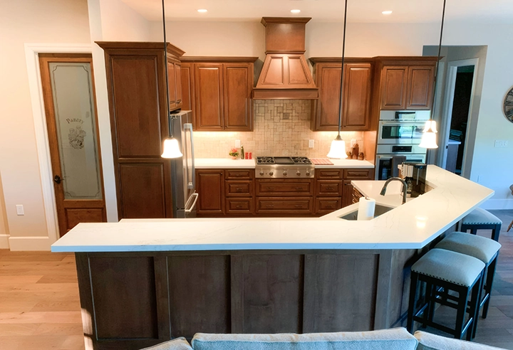 A modern kitchen featuring brown wooden cabinetry, a white countertop, and pendant lighting, showcasing the quality work by Cal Pro Trim & Finish in Sacramento.