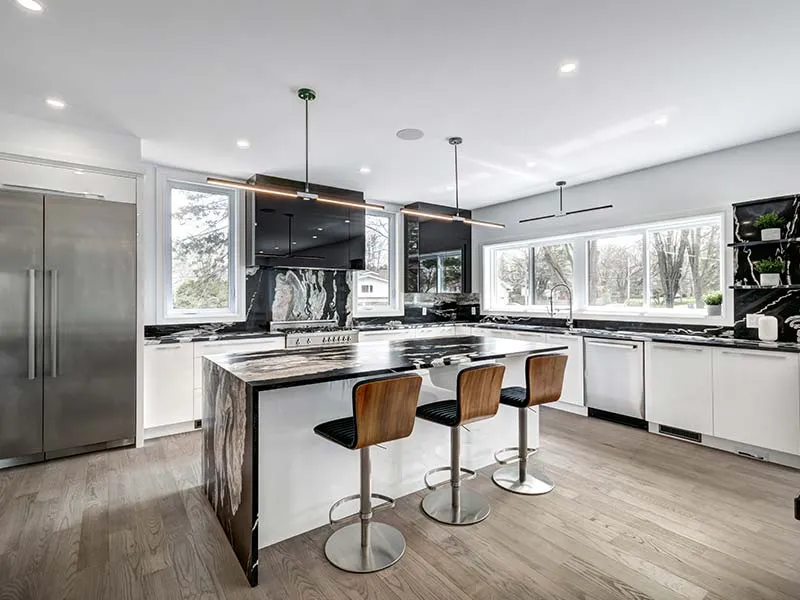 A modern kitchen with a large marble island, three high chairs, stainless steel appliances, and large windows, designed by Cal Summit Builders in San Rafael.