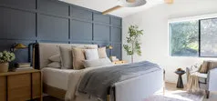 Modern bedroom with a dark accent wall, cozy bedding, a leafy plant, and a large window allowing natural light.