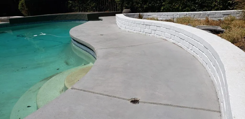 A concrete poolside area with a smooth overlay and a curved white brick wall, crafted by California Concrete Overlay Inc. in Martinez.