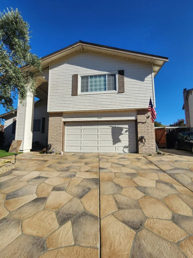 A house with a uniquely patterned concrete driveway, featuring a two-car garage with white doors, and an American flag on the right side.