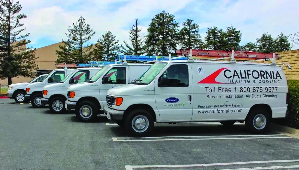A row of California Heating and Cooling service vans parked in a lot, equipped with red ladders on top, displaying company information and logo.